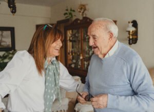 Elderly father and adult daughter sharing loving laughter - Oran Care - Oran Care Two smiling adults, a caregiver and an elderly man, share a laugh indoors in a home setting.
